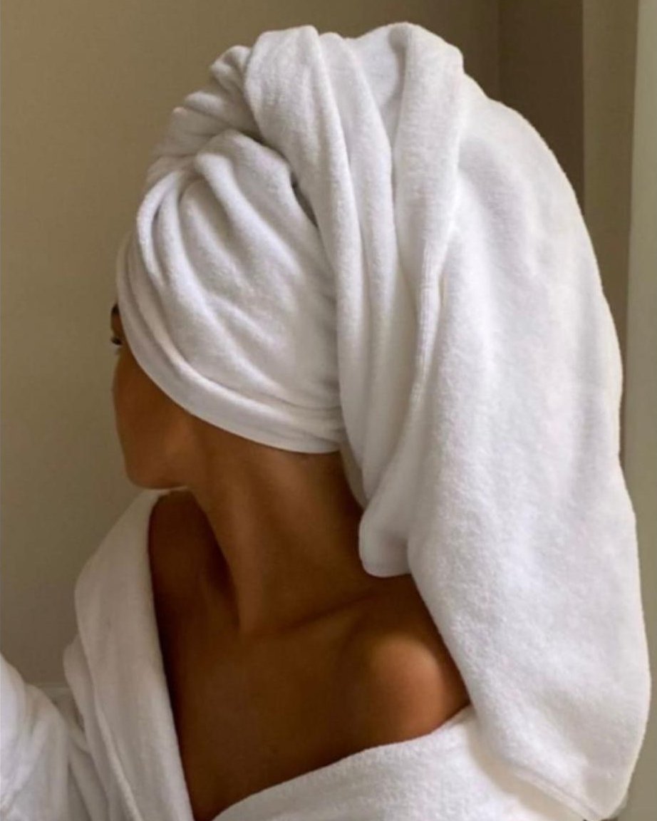Femme de dos, cheveux enveloppés dans une serviette blanche, peignoir sur les épaules